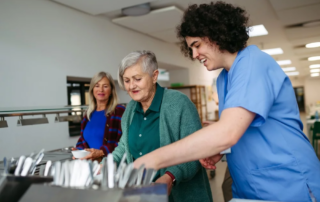Caregiver helping older woman in community center cafeteria.