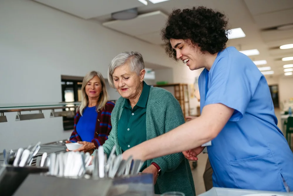 Caregiver helping older woman in community center cafeteria.